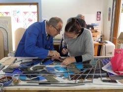 Un travail d'équipe pour ajuster et insérer les pièces de verre dans le plomb.