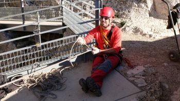 Le pompier fait lentement glisser la corde. Il est assis, le point fixe étant situé à la base du poteau du garde corps