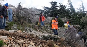 Les pierres sont alignées à côté du muret à prolonger. Eric taille un arbuste